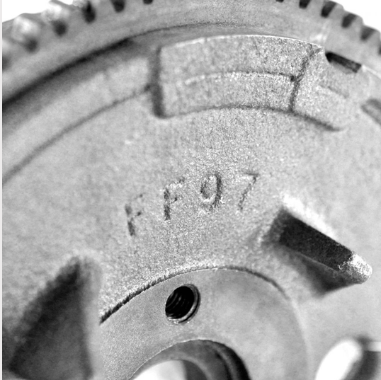 Flywheel kit and puller in metallic gray, close-up view of gear with stamped markings