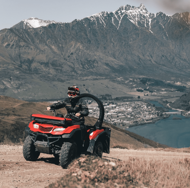 Red ATV quad bike with rider on a dirt trail, rugged mountains and lake in the background.