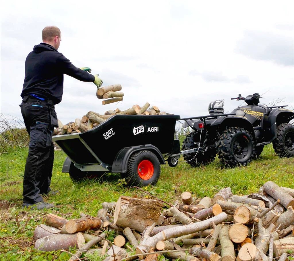 JFC Agri ATV hydraulic tipping trailer, 500 kg capacity, black; hitched to an ATV as a man loads firewood.