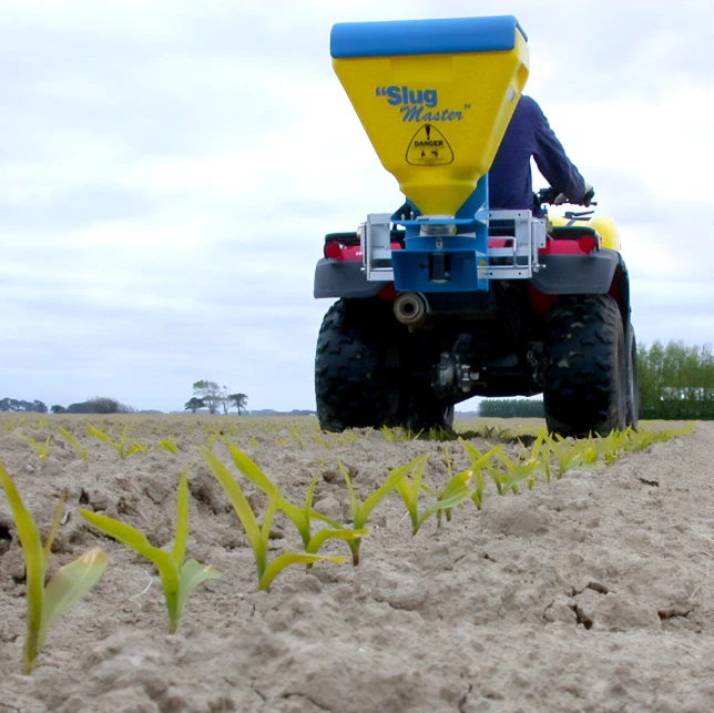 C-Dax SlugMaster SM75 spreader with yellow hopper and blue top mounted on ATV in a field