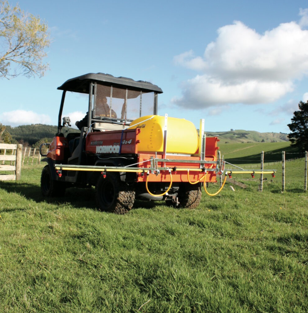 C-Dax spray-on sprayer on ATV with yellow tank and long orange boom arms in a grassy field.