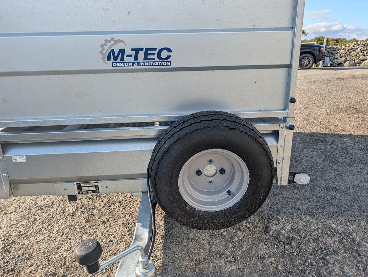 M-Tec quad master trailer with flip top, silver utility trailer with logo on side and spare wheel visible.