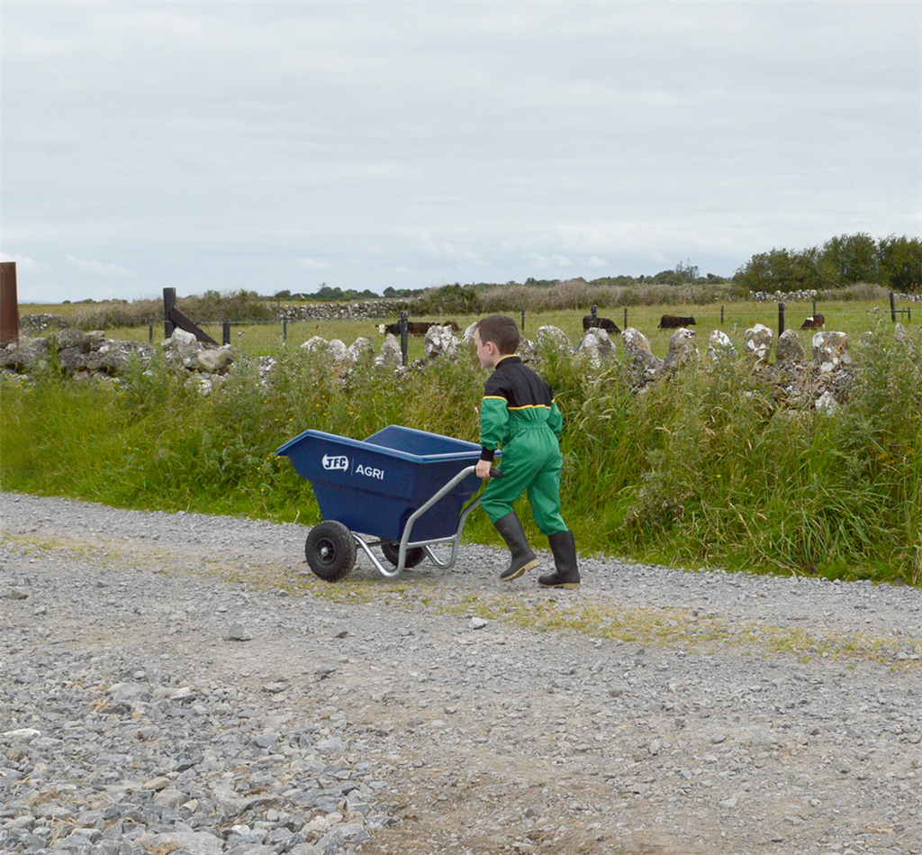 Junior 125L tipping wheelbarrow blue by JFC Agri, puncture-proof wheels, being pushed by a child along a gravel path