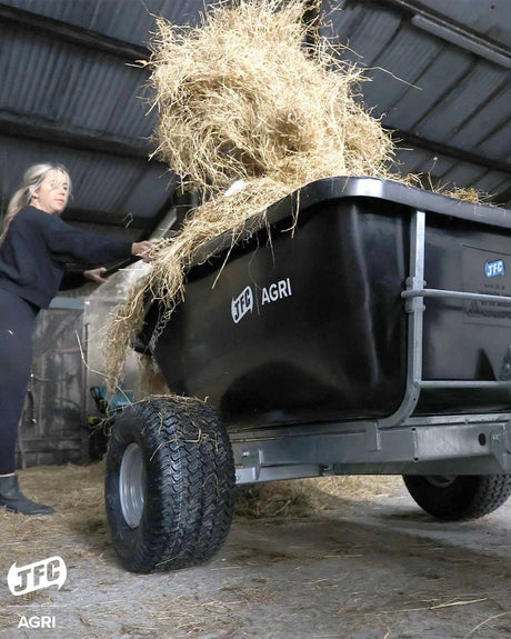 JFC Agri ATV tip trailer, black, loaded with hay inside a barn