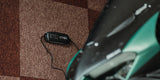 CTEK CT5 Powersport 12V battery charger, black, on a brown carpet beside a green vehicle