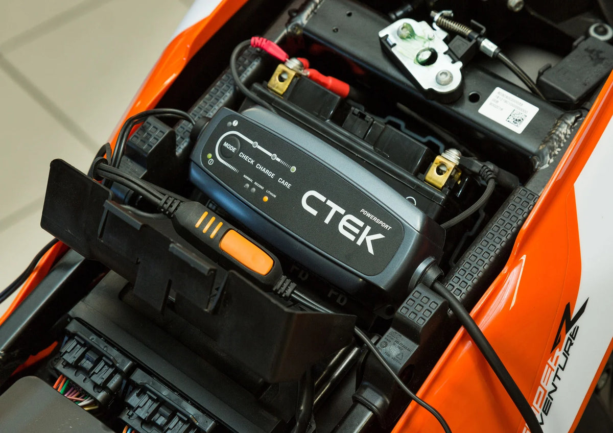 CTEK CT5 Powersport 12V battery charger installed in orange powersport vehicle with red/black clamps.