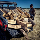 CFMOTO UTV bed loaded with stacked firewood; man wearing a cap and brown jacket stands nearby.