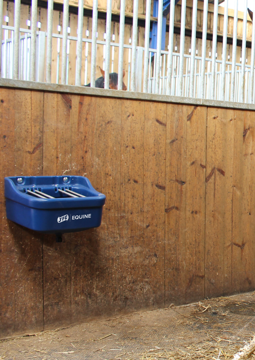 Blue JFC Equine foal creep feeder with adjustable stainless steel bars mounted on a wooden stall wall