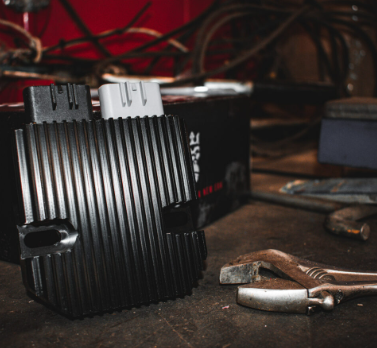 REVOLT regulator/rectifier by DGT Agri; black ribbed aluminum voltage regulator with dual connectors on a workbench.