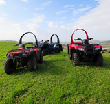 QuadGuard CPD & Mounting – Trax; three ATVs (red and blue) parked on a grassy field with hills in the distance.