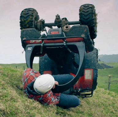 QuadGuard CPD & Mounting – Trax by DGT Agri, red; person in hard hat beneath an overturned ATV on a grassy field.