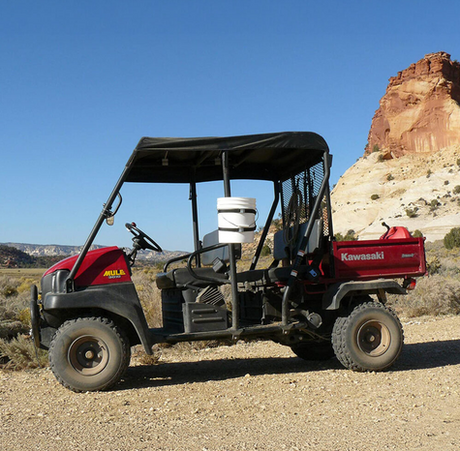 Bucket Binder - UTV, red Kawasaki Mule with black canopy and a white bucket in the cargo area, desert landscape behind