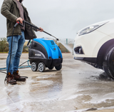 Pressure washer Hyundai blue and black with wheels, used to wash a car outdoors.