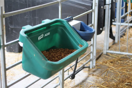 Green JFC Agri gate feed trough attached to a metal gate, containing livestock feed