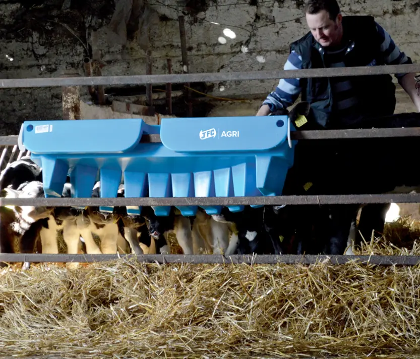 Blue JFC Agri 10-teat calf feeder with compartments mounted in a barn, surrounded by straw.