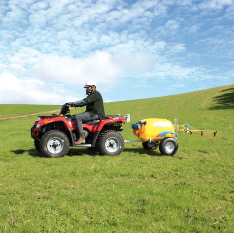 C-Dax Spray-On 200 Trailer Kit attached to red ATV and yellow sprayer trailer in a grassy field, two-item setup.