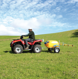 C-Dax ATV sprayer Gen 2 with yellow spray tank hitched to a red ATV in a grassy field