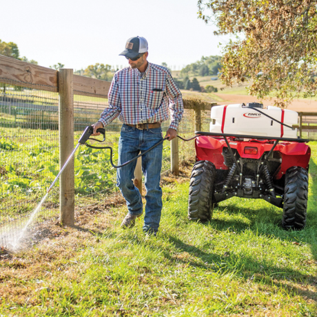 Fimco 25-Gallon Spot Sprayer LG25HV on ATV, white tank, 15 ft hose, spraying along fence.