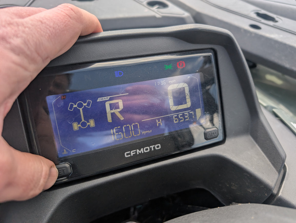 Used CFMOTO CFORCE 520 ATV instrument cluster with a hand on the housing; blue digital readout