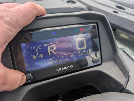Used CFMOTO CFORCE 520 ATV instrument cluster with a hand on the housing; blue digital readout