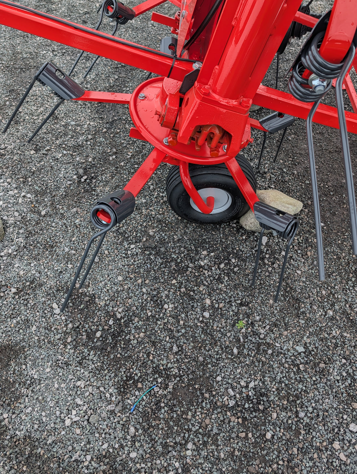 Kuhn GF582 6-rotor tedder for straw hay and silage, red frame with black tines and wheel on gravel.