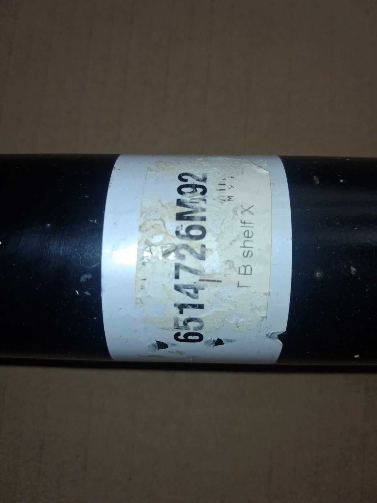 Shaft, black metal drive component with worn white label showing 6514726M92